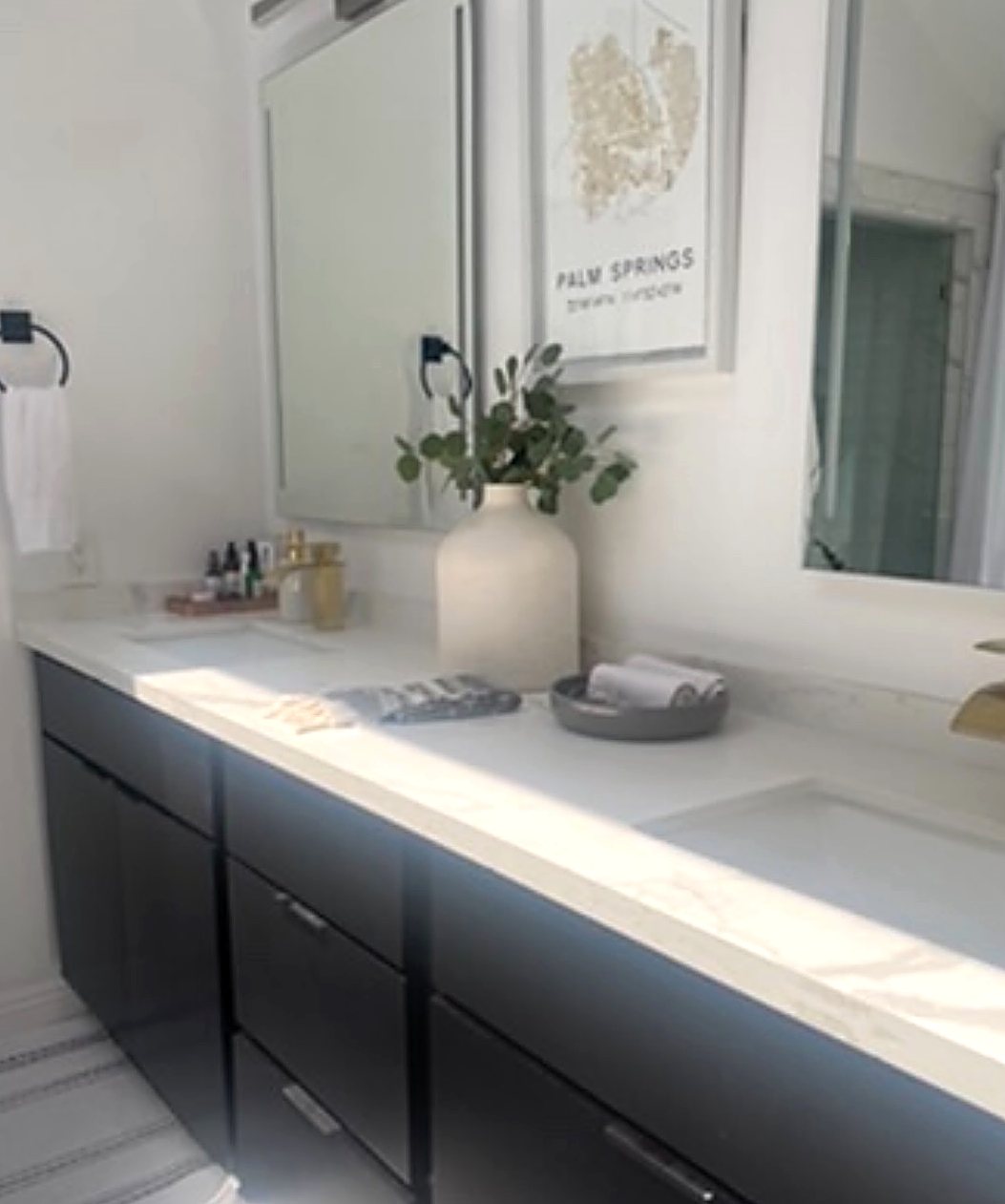Bathroom with a black double vanity, white quartz counter, brushed brass faucets and a vase of eucalyptus