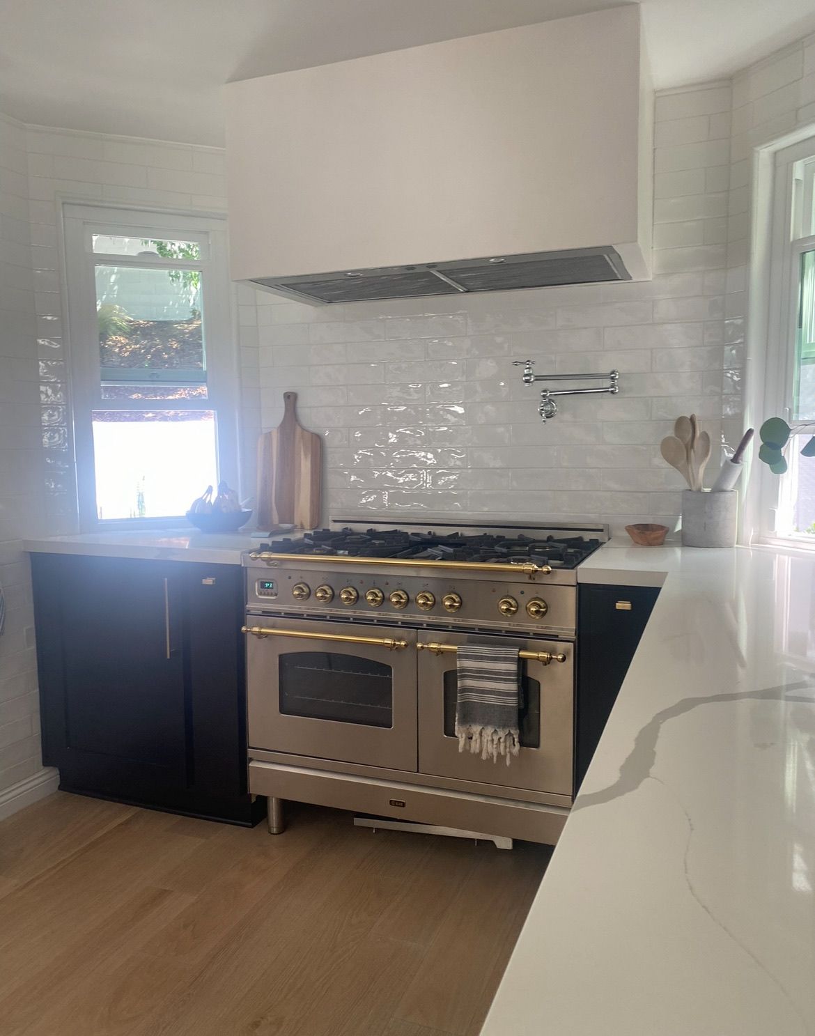 Kitchen with a stainless and brass range, plaster hood, hand-glazed white tile and black cabinetry