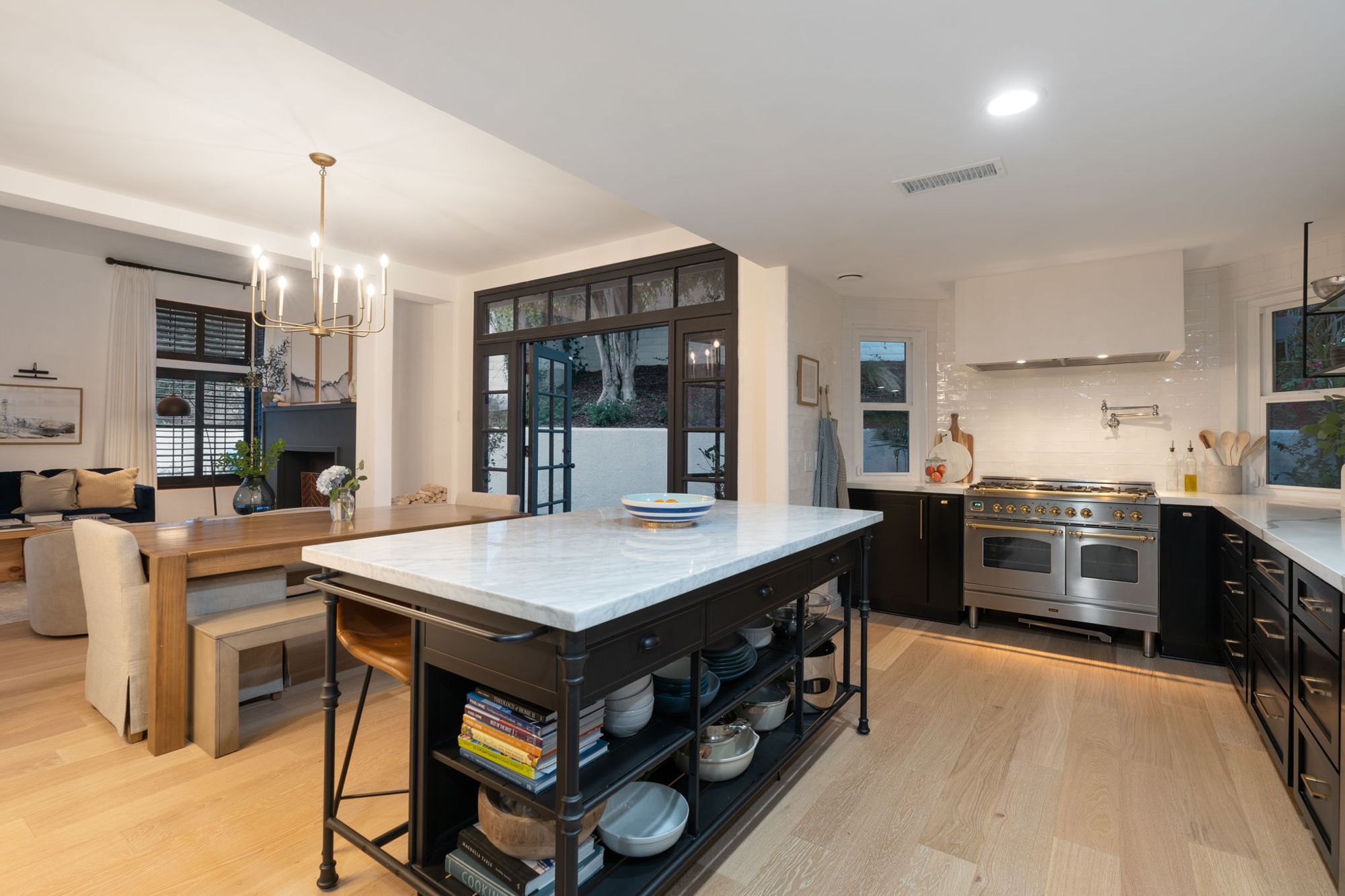 Kitchen with a marble-topped iron island with open shelving, black cabinetry, brass-trimmed range and steel French doors to the garden