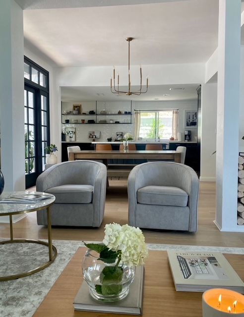 Pair of grey swivel chairs facing an open dining and kitchen area with a brass chandelier